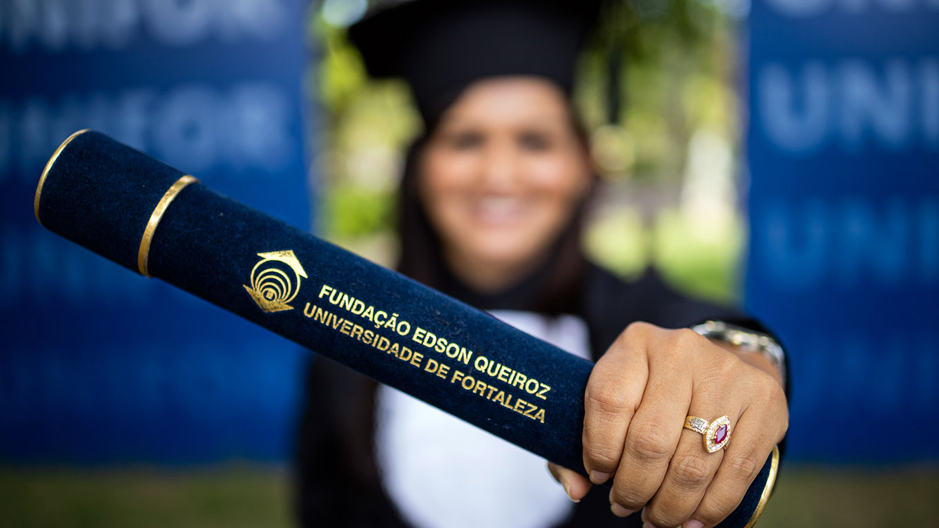 Uma mãe de uma aluna vestida de beca e segurando o diploma