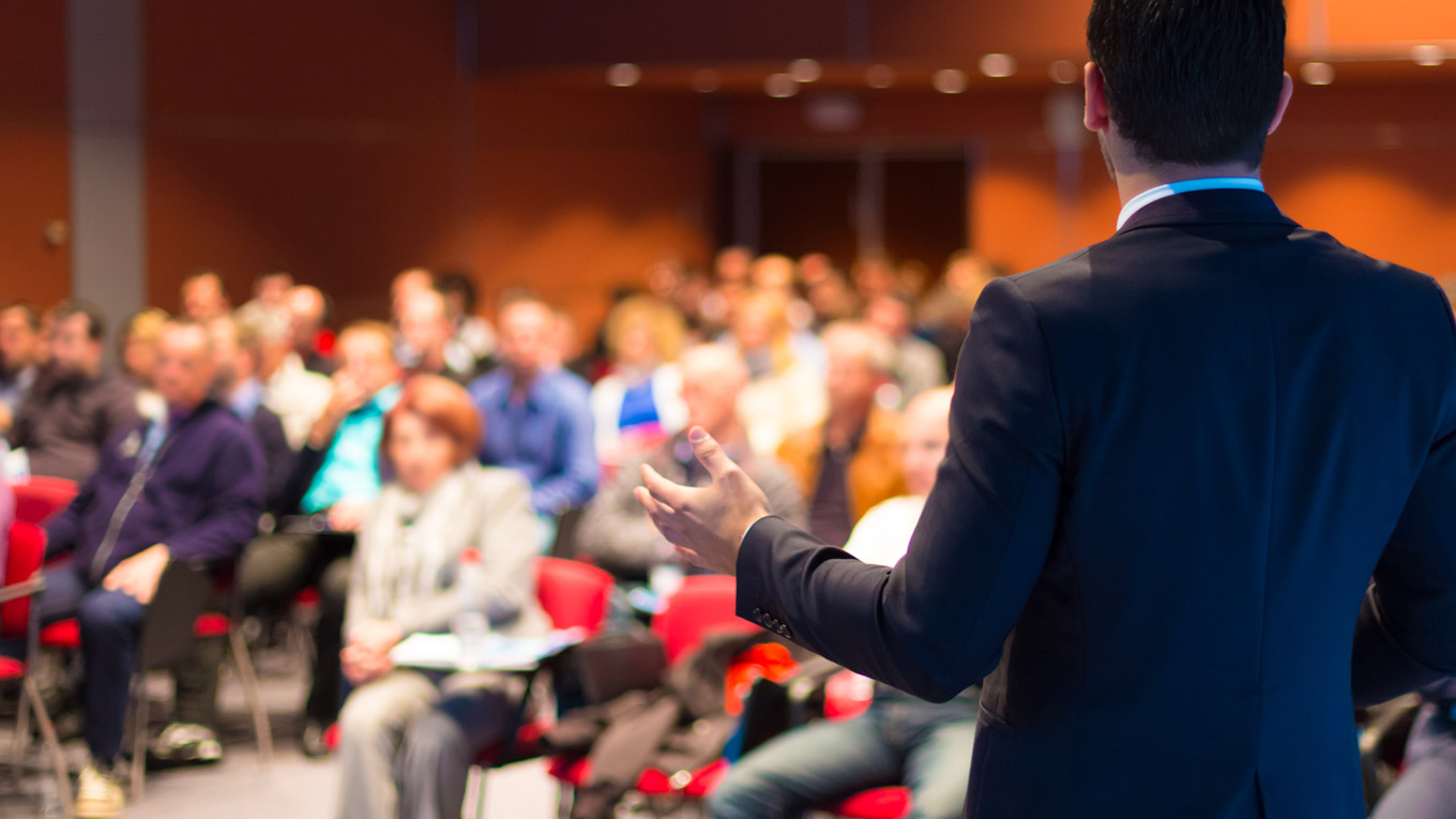 Um palestrante dá uma palestra para um público numeroso num auditório.