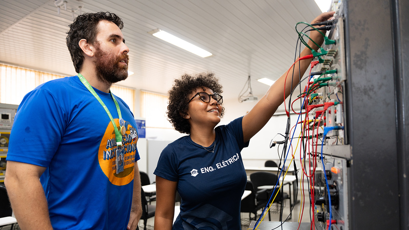 Estudante segura equipamento simulador enquanto professor aponta para detalhes