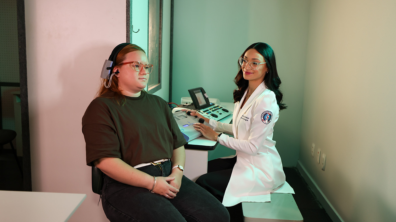 Paciente está dentro de uma cabine enquanto é atendido por fonoaudióloga