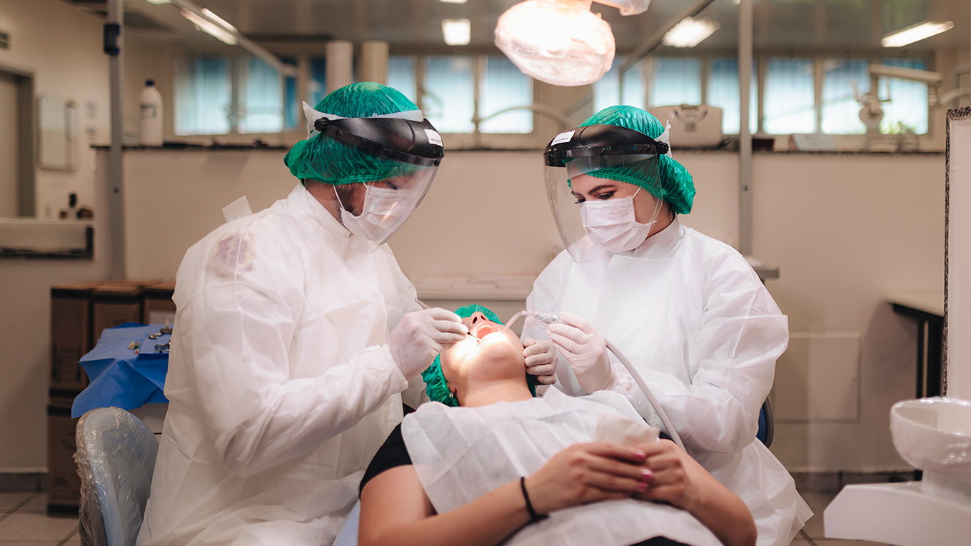 Dois dentistas atendem paciente no consultório odontológico