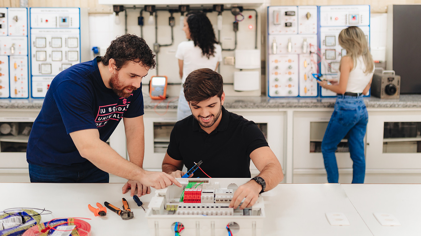 Estudante segura equipamento simulador enquanto professor aponta para detalhes