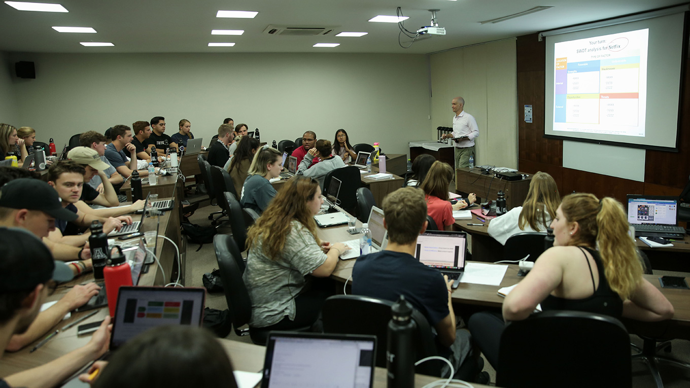 Estudantes sentados acompanham professor durante a aula.