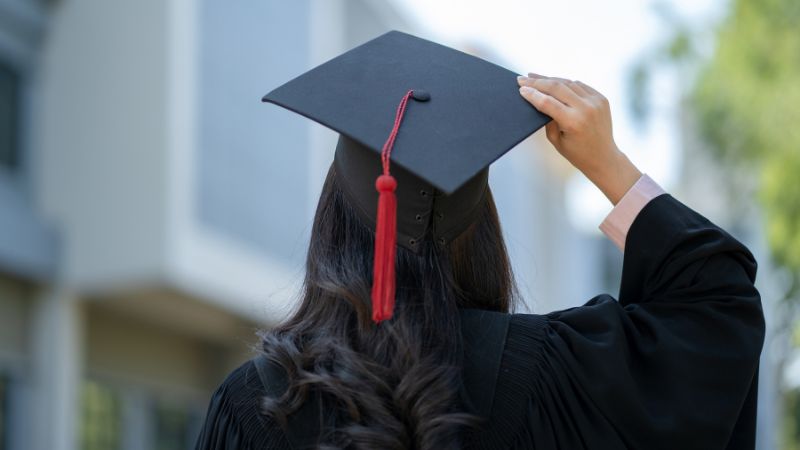 De costas, estudante segura chapéu de formatura