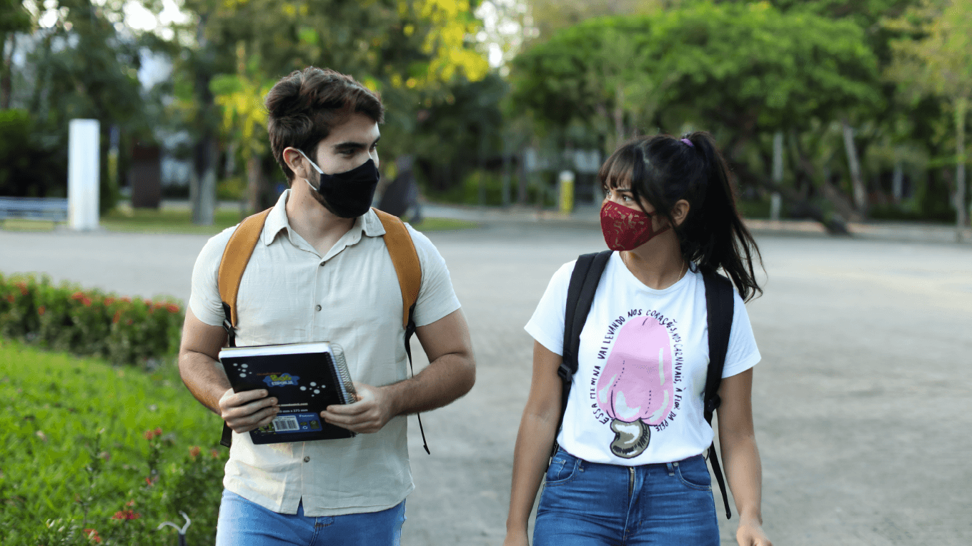 Dois amigos, de máscara, andando pelo campus