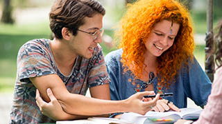 dois alunos, um rapaz e uma moça, sentados no banco ao ar livre na Unifor