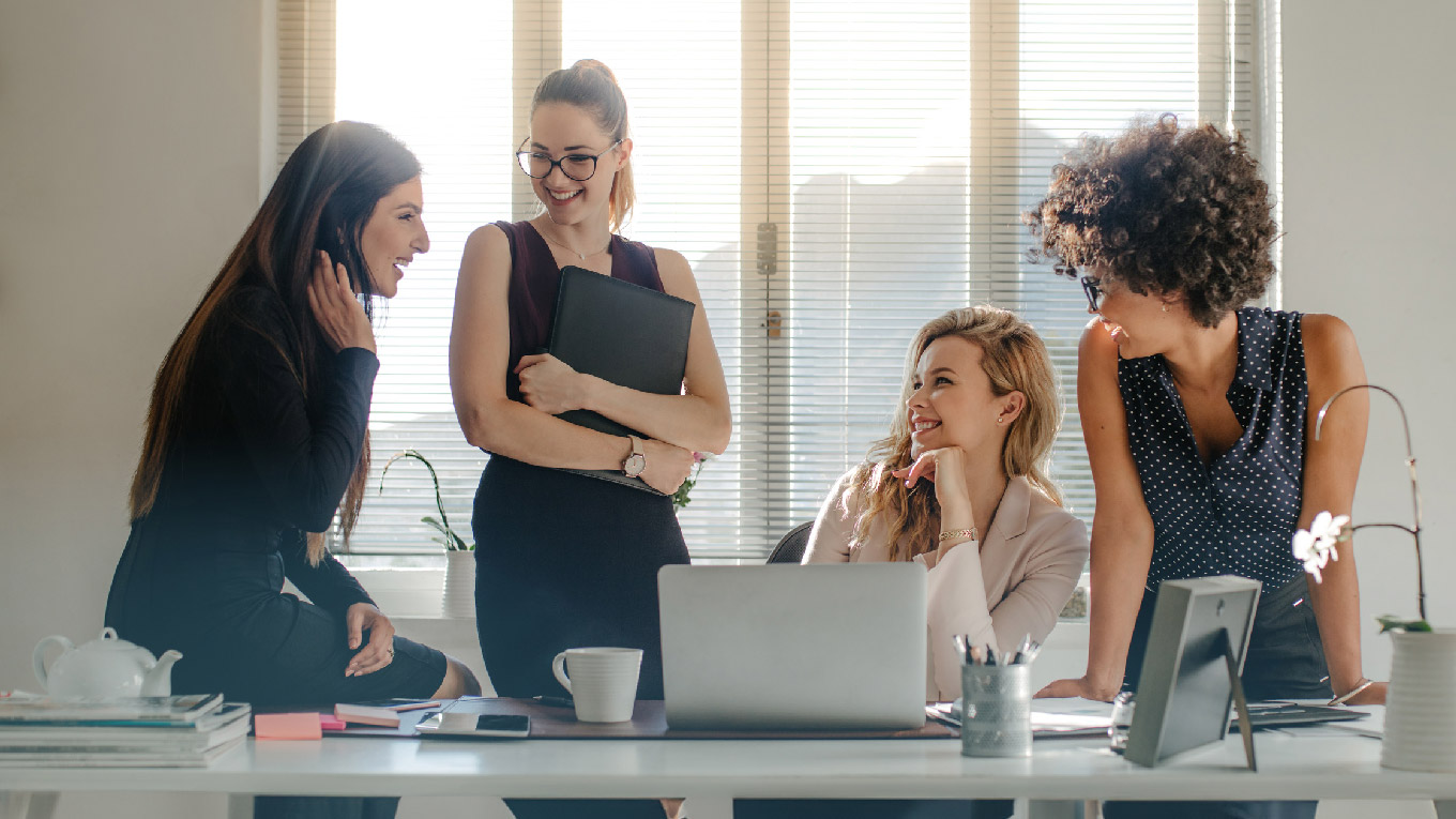 quatro mulheres ao redor de uma mesa de trabalho