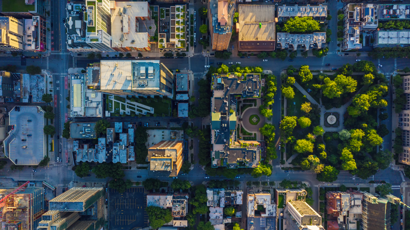 Imagem panorâmico do alto mostrando um um conjunto de prédios e uma praça arborizada.