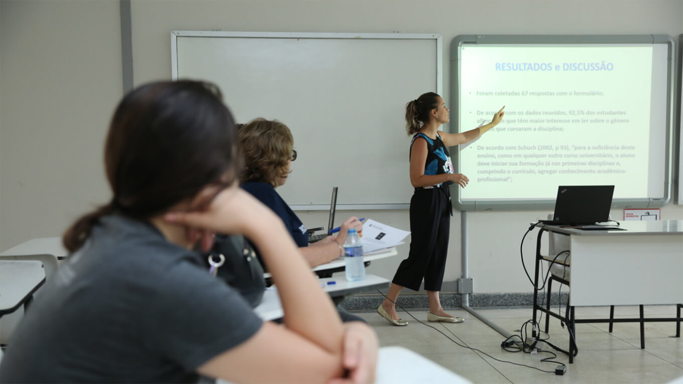 Uma estudante aponta para um quadro enquanto outros assistem.