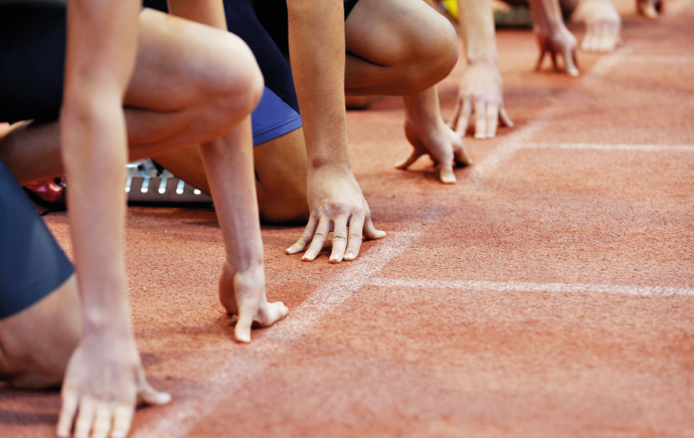 Atletas de corrida na linha de partida em uma pista de atletismo.