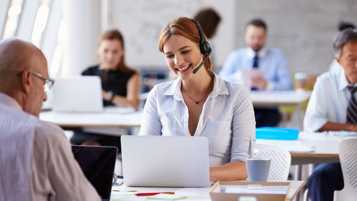 Profissional atende cliente por telefone em bancada com computador.